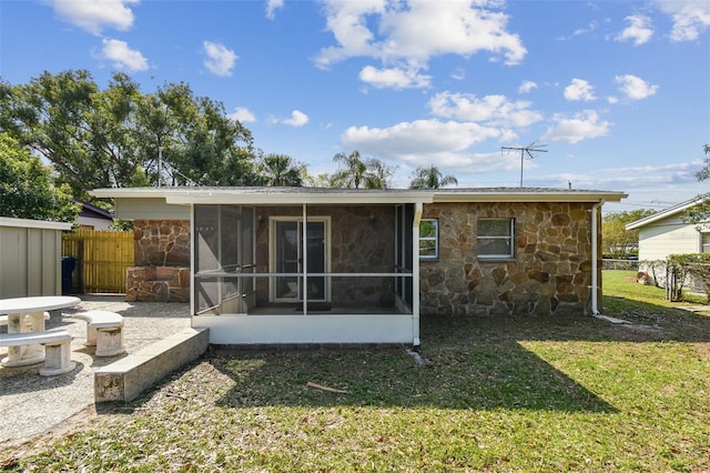 rear view of property featuring stone siding, a sunroom, a yard, and fence