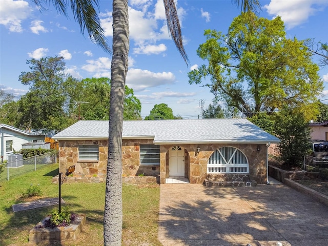 view of front of house with a front lawn, fence, roof with shingles, stone siding, and driveway