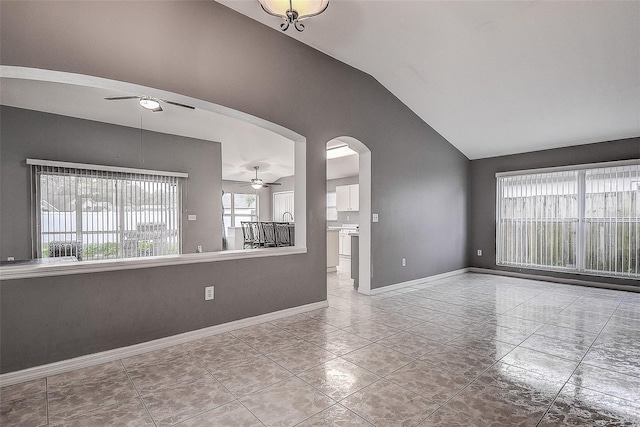 unfurnished living room featuring ceiling fan, arched walkways, vaulted ceiling, and baseboards