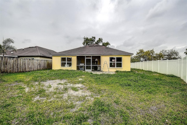 back of property with a sunroom, a fenced backyard, a yard, and stucco siding