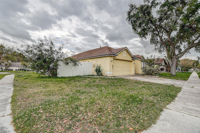 view of home's exterior with an attached garage, fence, concrete driveway, a lawn, and stucco siding