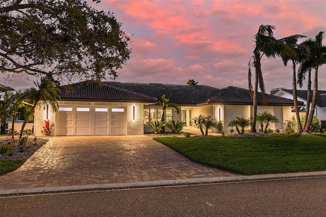 view of front of property featuring an attached garage, a tiled roof, decorative driveway, stucco siding, and a front lawn