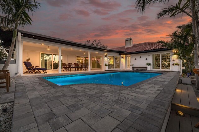 pool at dusk featuring an outdoor pool and a patio