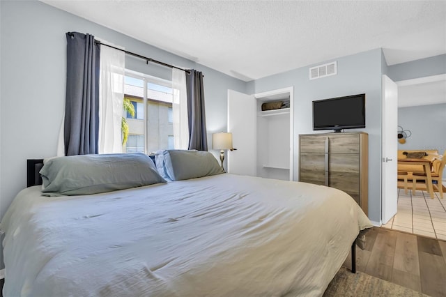 bedroom with a textured ceiling, a closet, wood finished floors, and visible vents