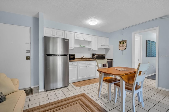 kitchen featuring range with electric cooktop, freestanding refrigerator, under cabinet range hood, a sink, and light tile patterned flooring