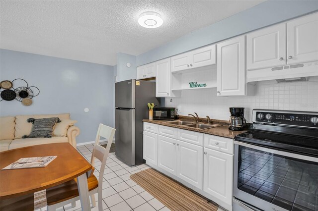 kitchen featuring light tile patterned flooring, under cabinet range hood, a sink, appliances with stainless steel finishes, and decorative backsplash