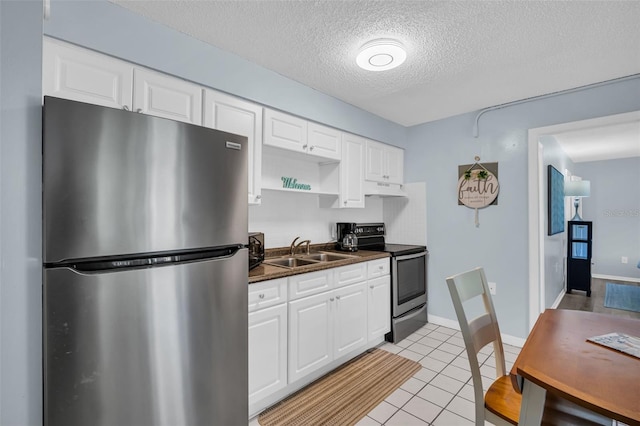 kitchen with light tile patterned floors, dark countertops, appliances with stainless steel finishes, white cabinetry, and a sink