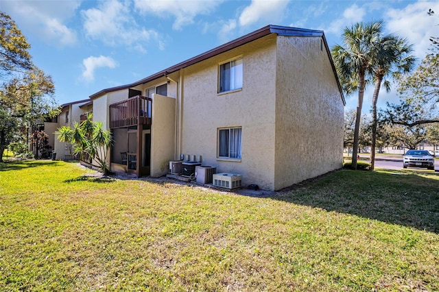 back of property featuring a balcony, stucco siding, central air condition unit, and a yard