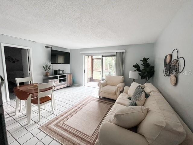 living area featuring light tile patterned flooring, visible vents, and a textured ceiling