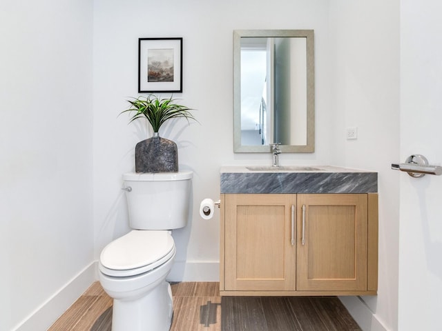 half bath with toilet, baseboards, wood finished floors, and vanity