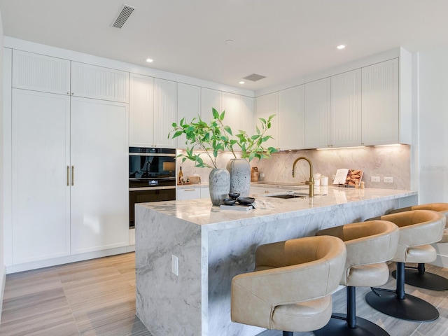 kitchen with oven, a sink, visible vents, light stone countertops, and tasteful backsplash