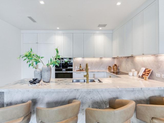 kitchen with light stone countertops, a sink, decorative backsplash, and black appliances