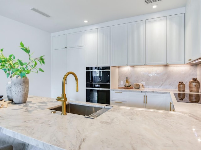 kitchen featuring a sink, visible vents, backsplash, light stone countertops, and black appliances