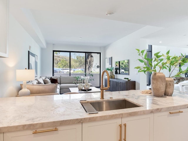 kitchen featuring open floor plan, light stone counters, a sink, and white cabinetry