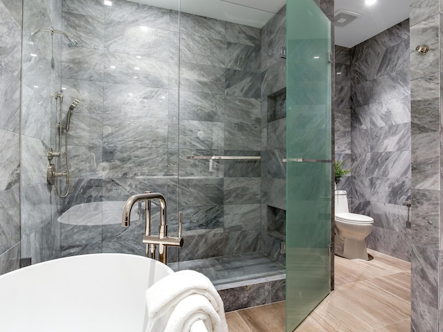 bathroom featuring toilet, a soaking tub, a shower stall, and tile walls