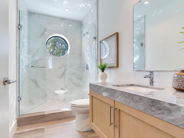 bathroom featuring toilet, a marble finish shower, and vanity