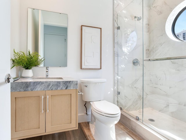 bathroom with toilet, vanity, a marble finish shower, and wood finished floors