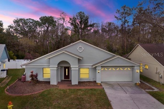 single story home featuring an attached garage, fence, concrete driveway, a lawn, and stucco siding