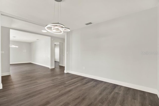 unfurnished room with dark wood-style flooring, visible vents, baseboards, and an inviting chandelier