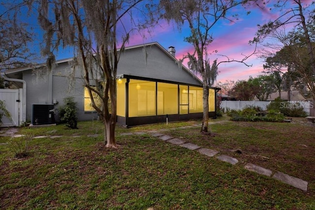 back of house at dusk featuring a sunroom, fence, a lawn, and central AC unit