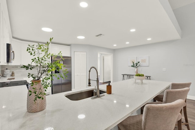 kitchen with a breakfast bar area, stainless steel appliances, visible vents, white cabinets, and a sink