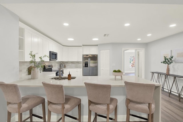 kitchen with light wood finished floors, open shelves, stainless steel appliances, a sink, and a peninsula