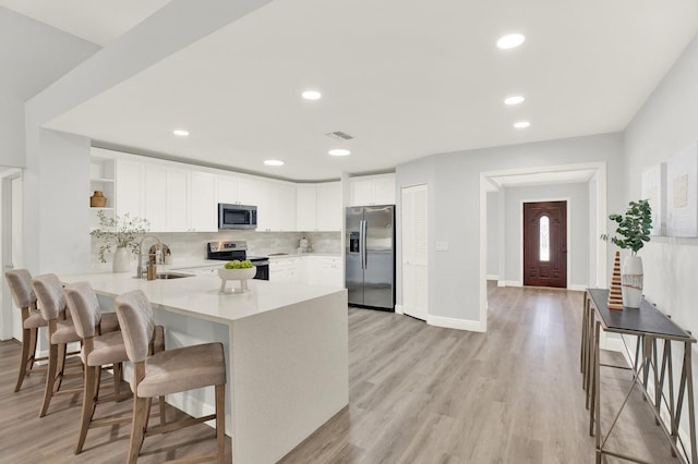 kitchen with light wood-style flooring, stainless steel appliances, a peninsula, backsplash, and open shelves