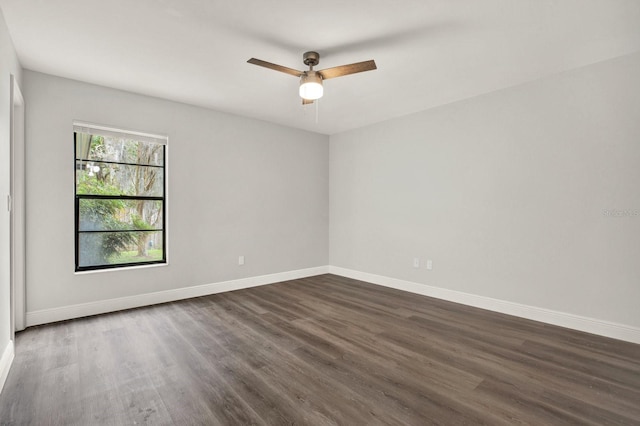 spare room featuring dark wood-style floors, a ceiling fan, and baseboards