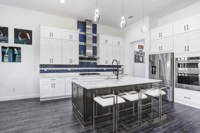 kitchen with a breakfast bar, stainless steel appliances, backsplash, dark wood-type flooring, and wall chimney range hood