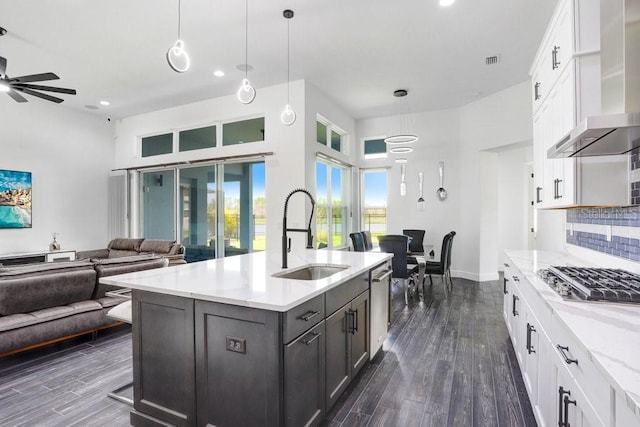 kitchen with stainless steel appliances, a sink, open floor plan, backsplash, and wall chimney exhaust hood