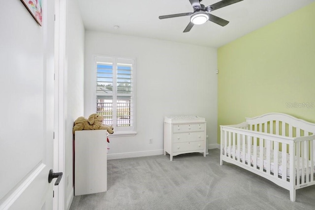 bedroom with a crib, carpet, a ceiling fan, and baseboards