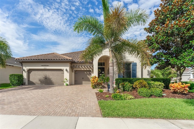 mediterranean / spanish home with an attached garage, a tiled roof, decorative driveway, and stucco siding