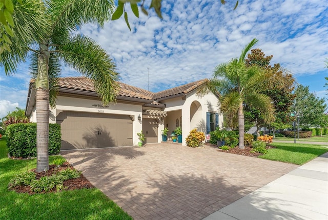 mediterranean / spanish house with a garage, a tile roof, decorative driveway, and stucco siding