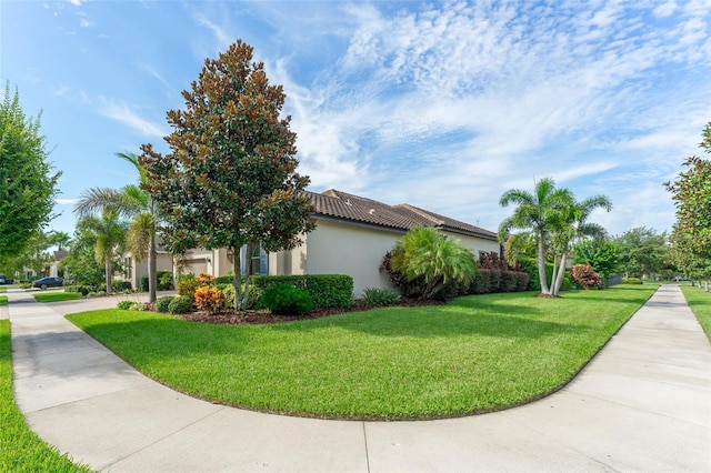 view of home's exterior featuring driveway, a tiled roof, an attached garage, a yard, and stucco siding