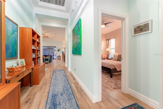 hallway featuring ornamental molding, light wood-style flooring, and baseboards