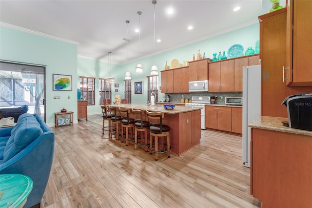 kitchen with crown molding, light wood finished floors, decorative backsplash, white appliances, and a kitchen bar