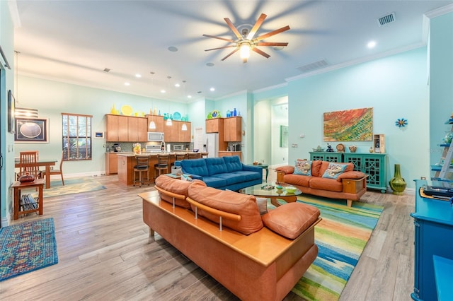 living area with light wood-style flooring, visible vents, baseboards, and ornamental molding