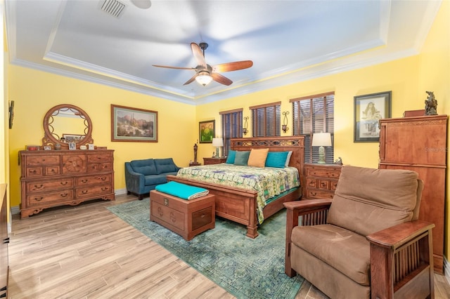 bedroom featuring a tray ceiling, light wood finished floors, visible vents, and crown molding