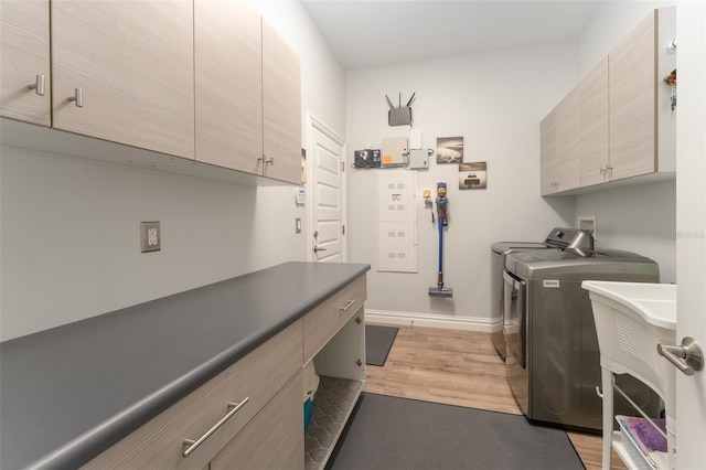 clothes washing area with light wood-style floors, washing machine and dryer, cabinet space, and baseboards