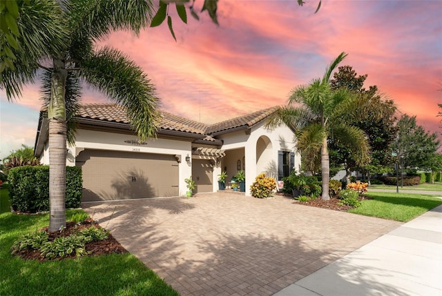 mediterranean / spanish house featuring a garage, decorative driveway, a tile roof, and stucco siding