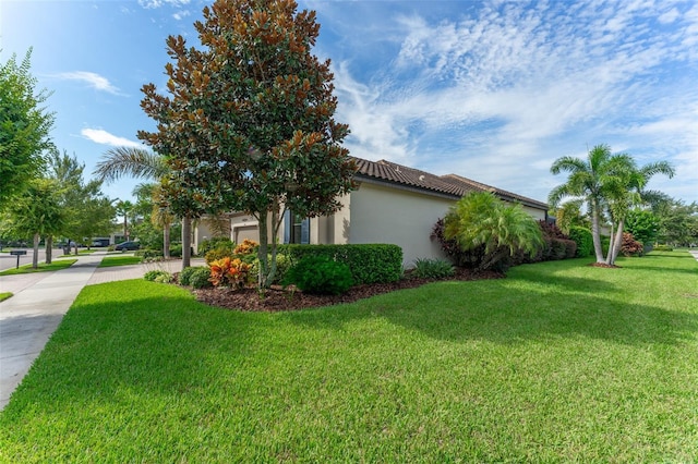 view of side of property with a garage, a tile roof, a yard, and stucco siding