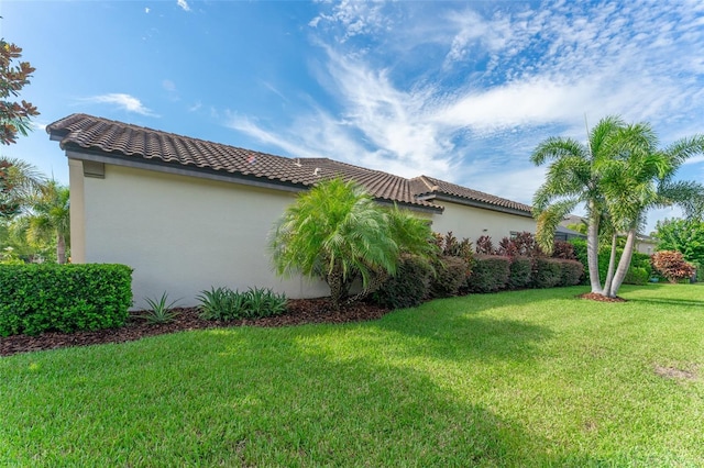 view of home's exterior featuring a tiled roof, a lawn, and stucco siding