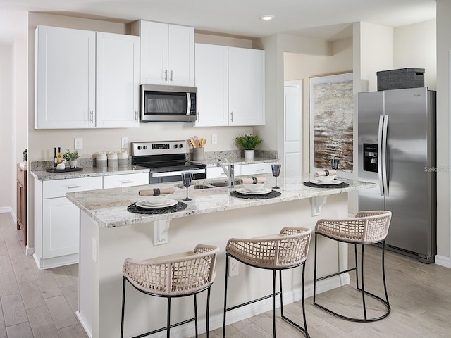 kitchen featuring light stone countertops, white cabinetry, light wood-style flooring, and appliances with stainless steel finishes