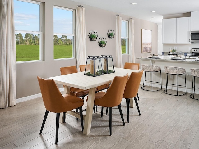 dining space featuring light wood finished floors, plenty of natural light, and baseboards