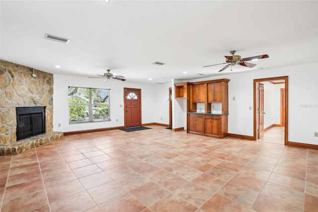 unfurnished living room with a stone fireplace, baseboards, visible vents, and a ceiling fan