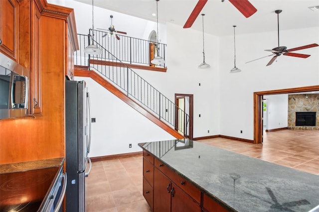 kitchen with visible vents, brown cabinets, a ceiling fan, a stone fireplace, and appliances with stainless steel finishes