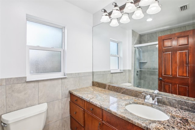 bathroom with visible vents, toilet, vanity, a stall shower, and tile walls