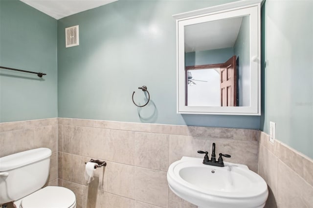 half bath featuring visible vents, a wainscoted wall, toilet, a sink, and tile walls