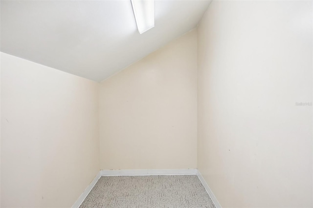 empty room with light carpet, baseboards, and vaulted ceiling