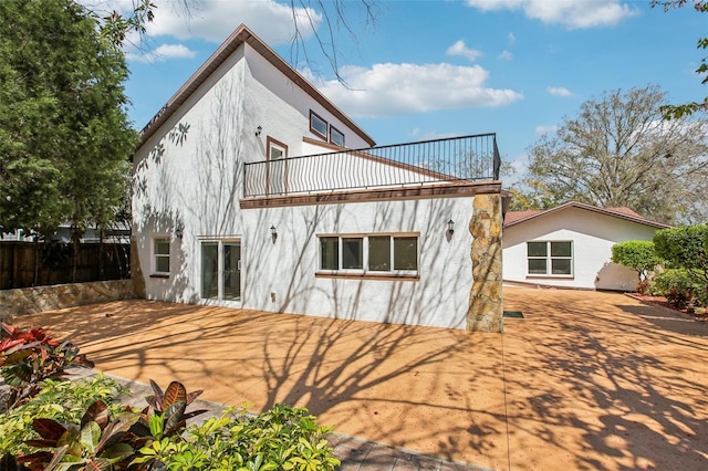 rear view of house featuring stucco siding, a balcony, and fence